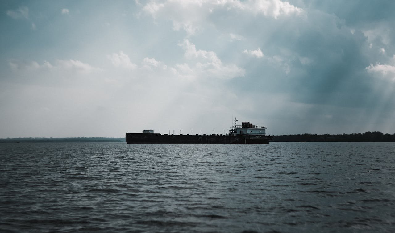 A cargo ship sails peacefully on the sea with dramatic clouds overhead.
